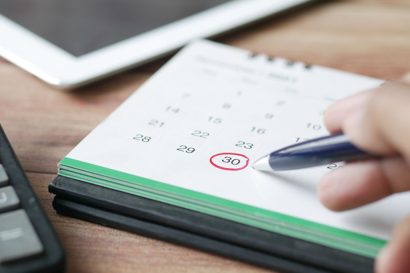 Une main tenant un stylo entoure le chiffre 30 sur un calendrier de bureau — « Quand chercher une formation en alternance ? Le meilleur moment » — tandis qu’une calculatrice et une tablette sont posées à l’arrière-plan.