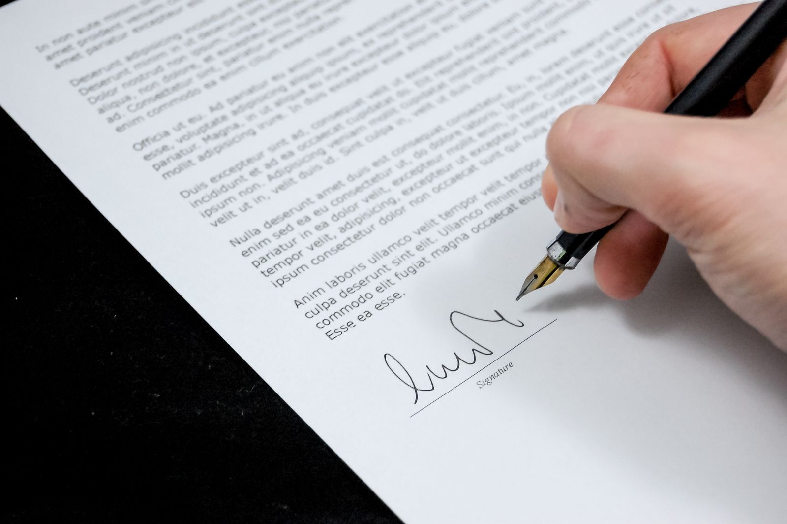 Une main tenant un stylo est en train de signer un document au bas de celui-ci, où l'on peut voir une signature et le mot « Signature ». Le document, probablement une lettre de motivation, est imprimé en noir sur du papier blanc.