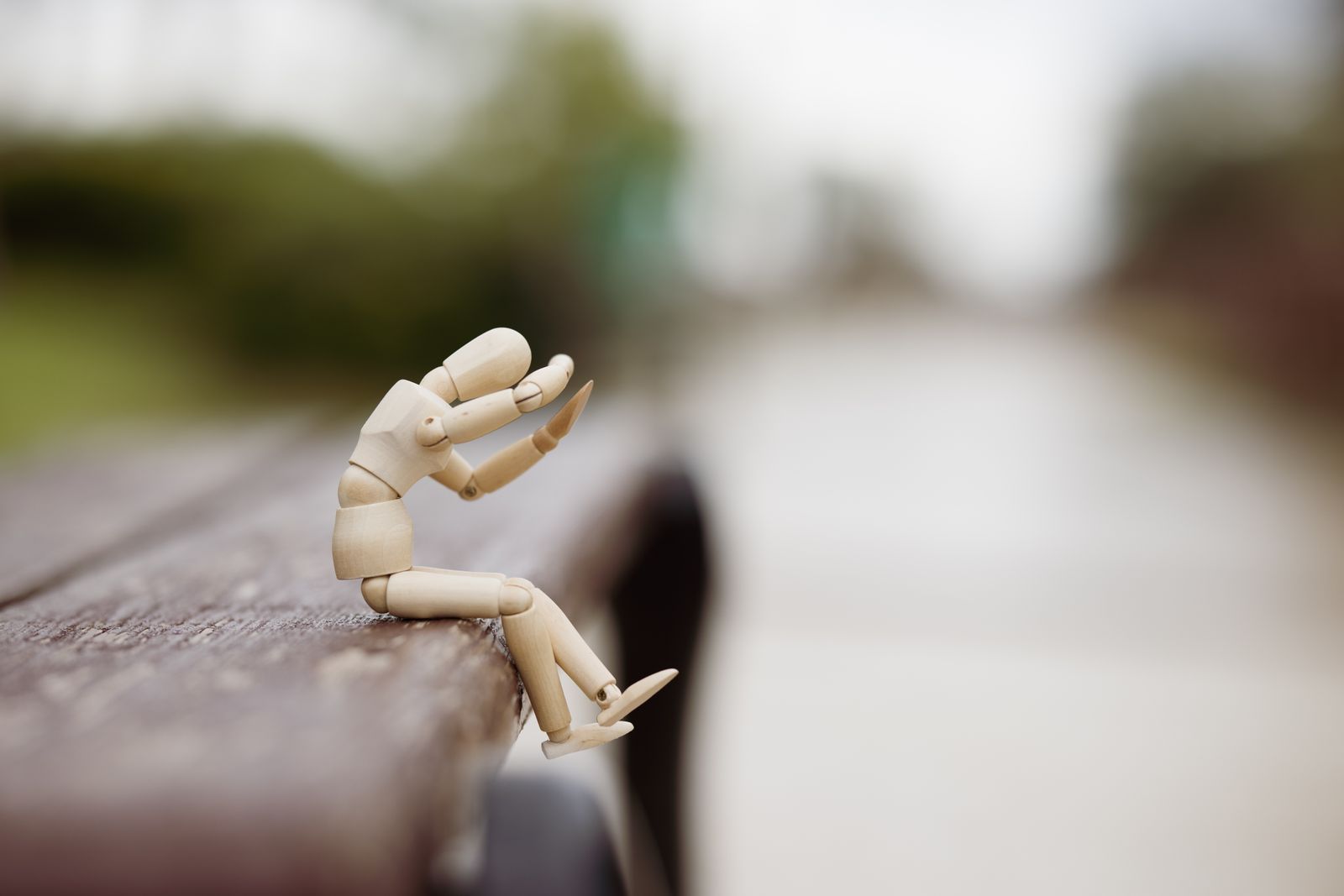 Un mannequin d'artiste en bois est assis sur le bord d'un banc à l'extérieur, comme sur une scène, penché en avant, les bras levés près de la tête, semblant exprimer de la détresse symbolisant "pas de stage trouvé". L'arrière-plan est flou.