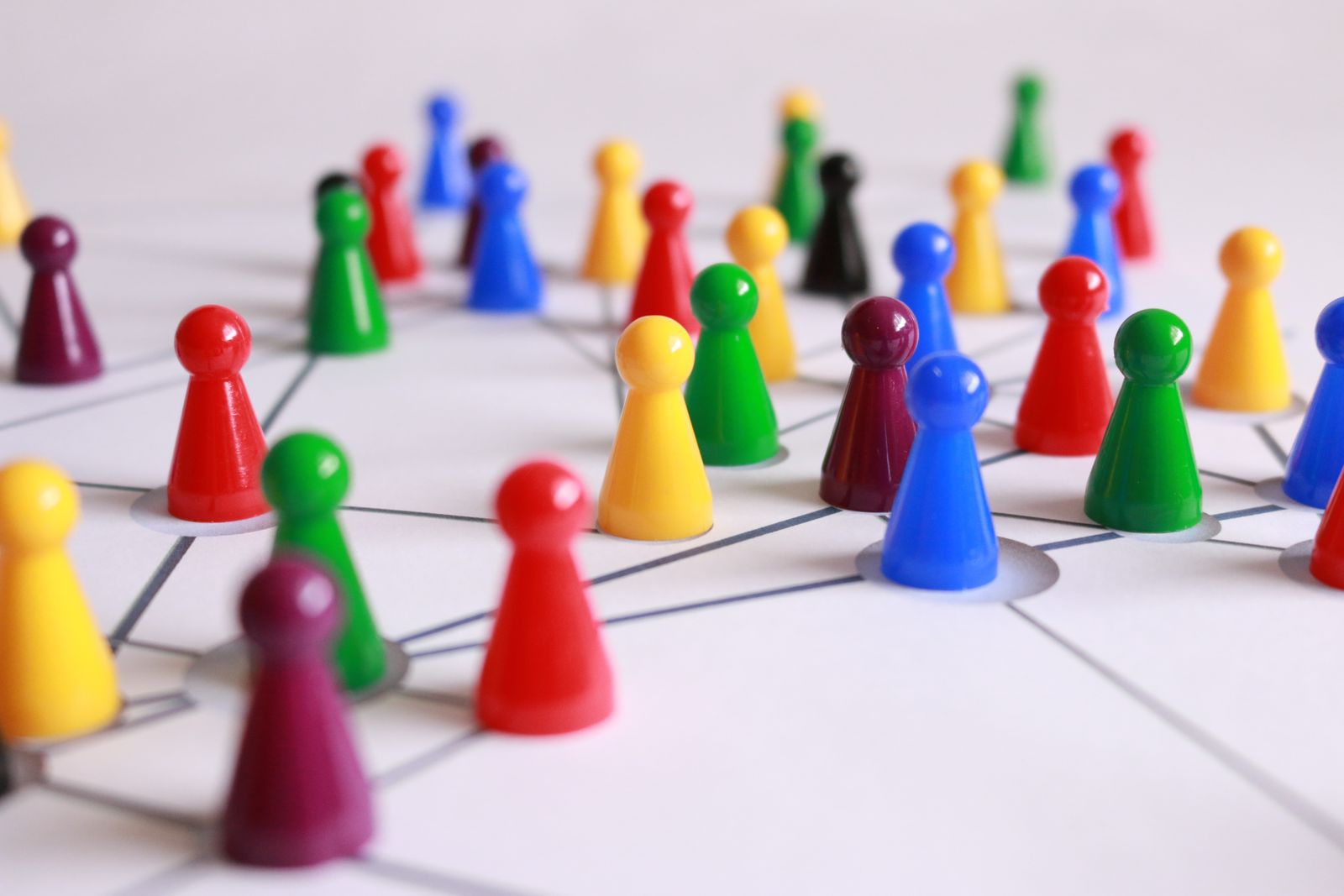 Des pions de jeu en plastique colorés sont disposés sur une surface blanche, reliés par des lignes noires formant un réseau, symbolisant la réussite d'une mobilité interne, le travail d'équipe et des liens professionnels solides.