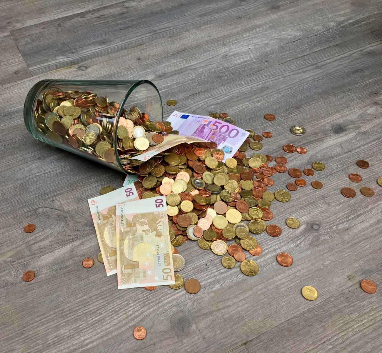 Un verre qui se renverse sur un parquet fait tomber des pièces et des billets en euros, notamment des billets de 500 et de 50 — à l’image des erreurs qui font perdre du salaire, de petites erreurs peuvent entraîner des pertes plus importantes.