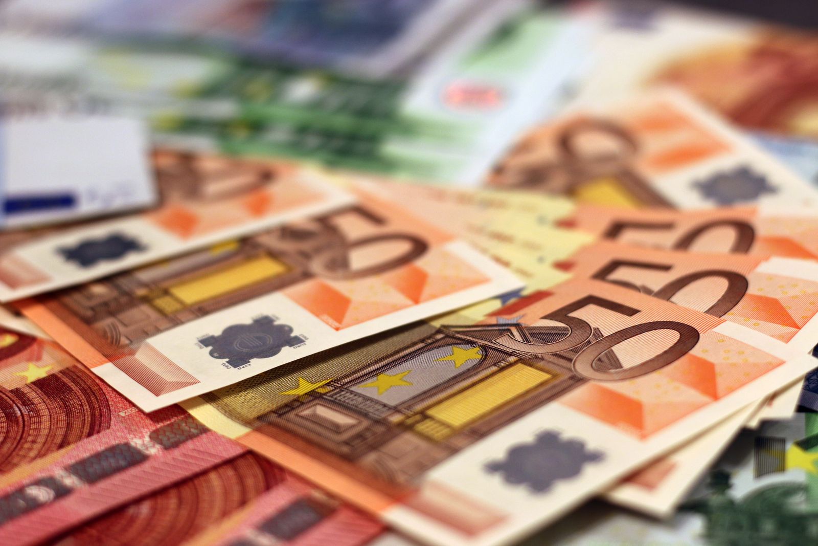 Gros plan sur plusieurs billets de 50 euros disposés en éventail, avec d'autres billets en arrière-plan, flous. Les billets arborent des motifs architecturaux et des éléments de sécurité — symboles des moyens de « gagner plus » et de sécuriser vos finances.
