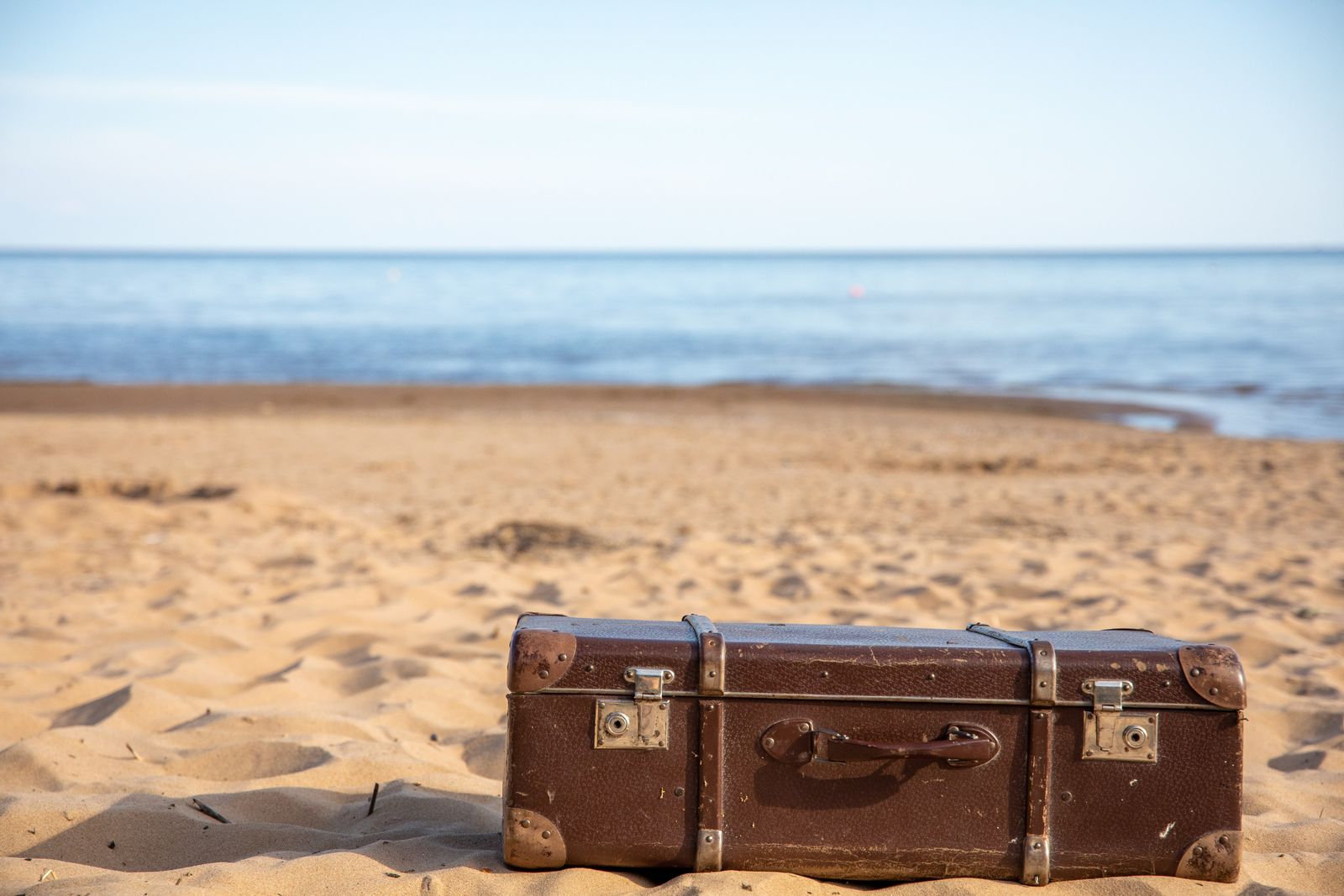 Une valise vintage marron repose sur une plage de sable, avec en arrière-plan une mer calme et un ciel limpide, évoquant un nouveau départ — une source d'inspiration idéale pour ceux qui cherchent à trouver un emploi sans diplôme.