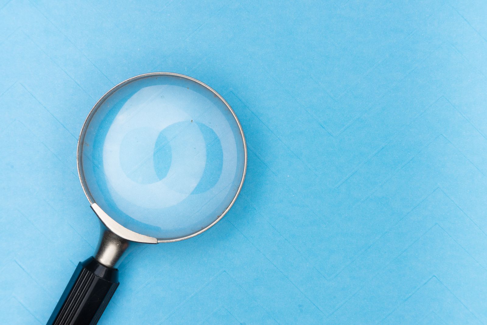 Une loupe au manche noir est posée sur une surface bleu clair, projetant une ombre discrète et révélant les détails d'un CV qui fait la différence dans le motif qui se trouve en dessous.
