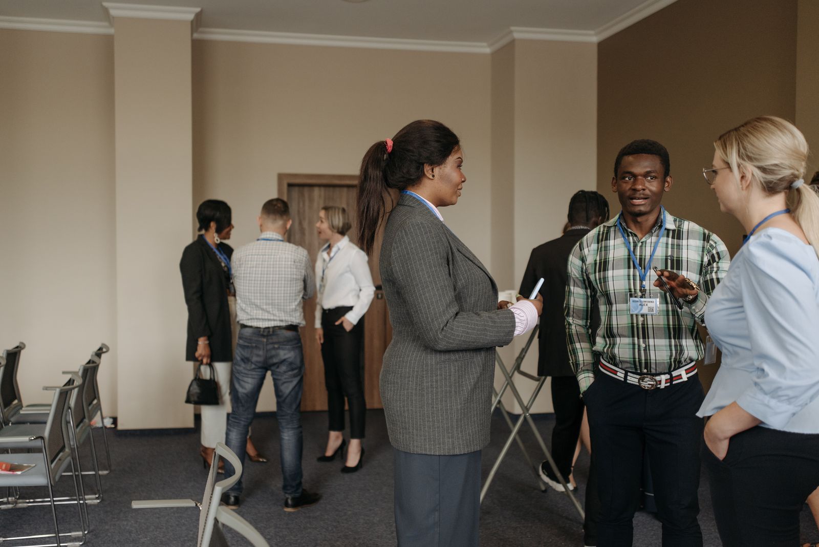 Dans une salle de conférence équipée de chaises, un groupe de personnes, vêtues de tenues professionnelles et portant des badges nominatifs, discutent par petits groupes afin d'élargir leur réseau professionnel.